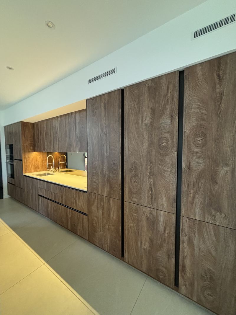 Mur de colonnes toute hauteur en décor bois foncé veiné, gorges noires verticales, niche de plan de travail avec crédence miroir et LED