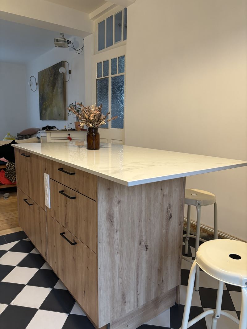 Îlot en décor chêne naturel (tiroirs à poignées noires) avec plan effet marbre blanc débordant, tabourets métal blanc
