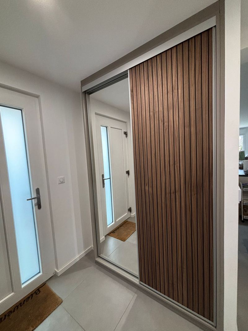 Placard d'entrée à portes coulissantes sous cadre alu : une porte miroir, une porte habillée de tasseaux verticaux bois foncé