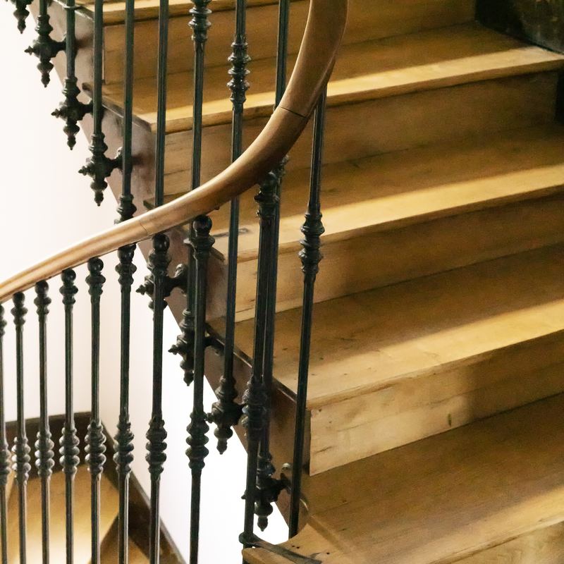 Escalier ancien : marches en chêne patiné, balustres en fonte ouvragée et main courante bois cintrée