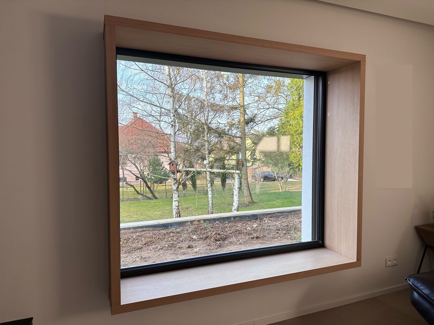Banquette de fenêtre : caisson profond en décor chêne habillant une grande baie à cadre noir, assise sur l'appui